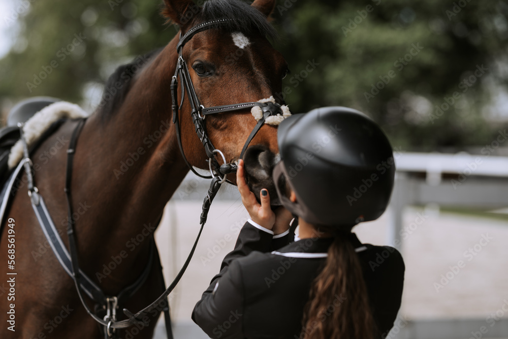 Attractive female equestrian in riding helmet looking at horse in horse club. Attractive female equestrian in riding helmet looking at horse in horse club.