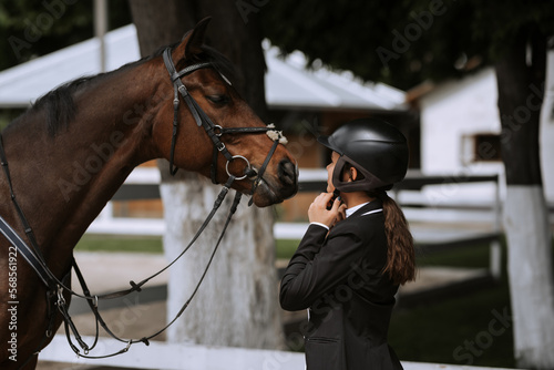 Attractive female equestrian in riding helmet looking at horse in horse club. © JJ Studio