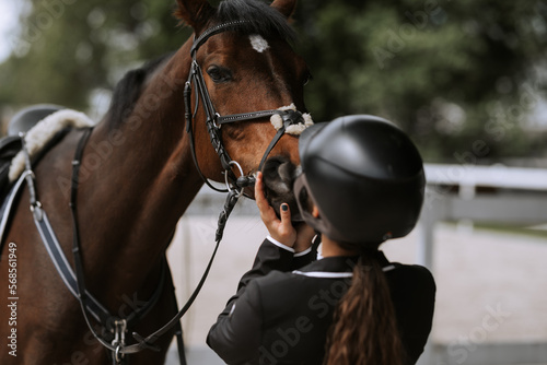 Attractive female equestrian in riding helmet looking at horse in horse club. © JJ Studio