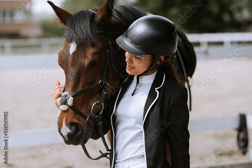Beautiful professional female jockey standing near horse. woman horse rider is preparing to equitation. girl and horse. equestrian sport concept. riding horse vacation