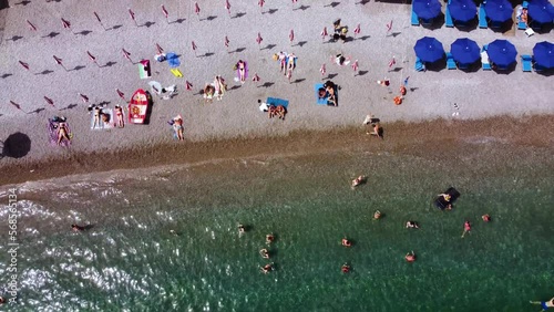 Aerial drone footage of the Marina Grande beach, town hall, Sant'Andrea duomo bell tower in Amalfi coast, Campania, Italy. Parasol, sun loungers, people swimming and colourful cliff villas from above.