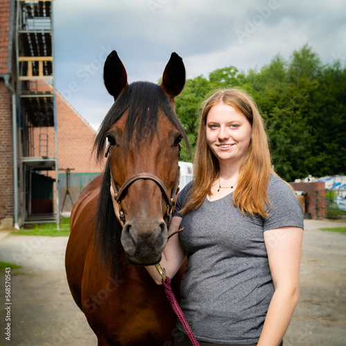 Junge Frau hält ihr Pferd am Zaumzeug auf einem Hof. © Countrypixel