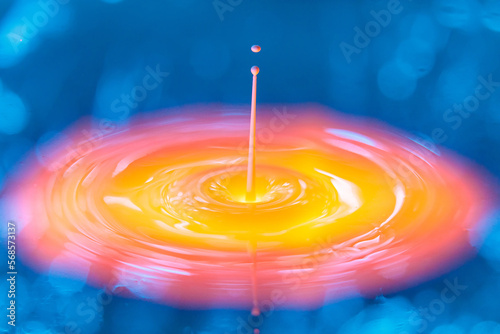 The drop falls into a dense liquid with a blue-yellow background. Abstract colorful background.