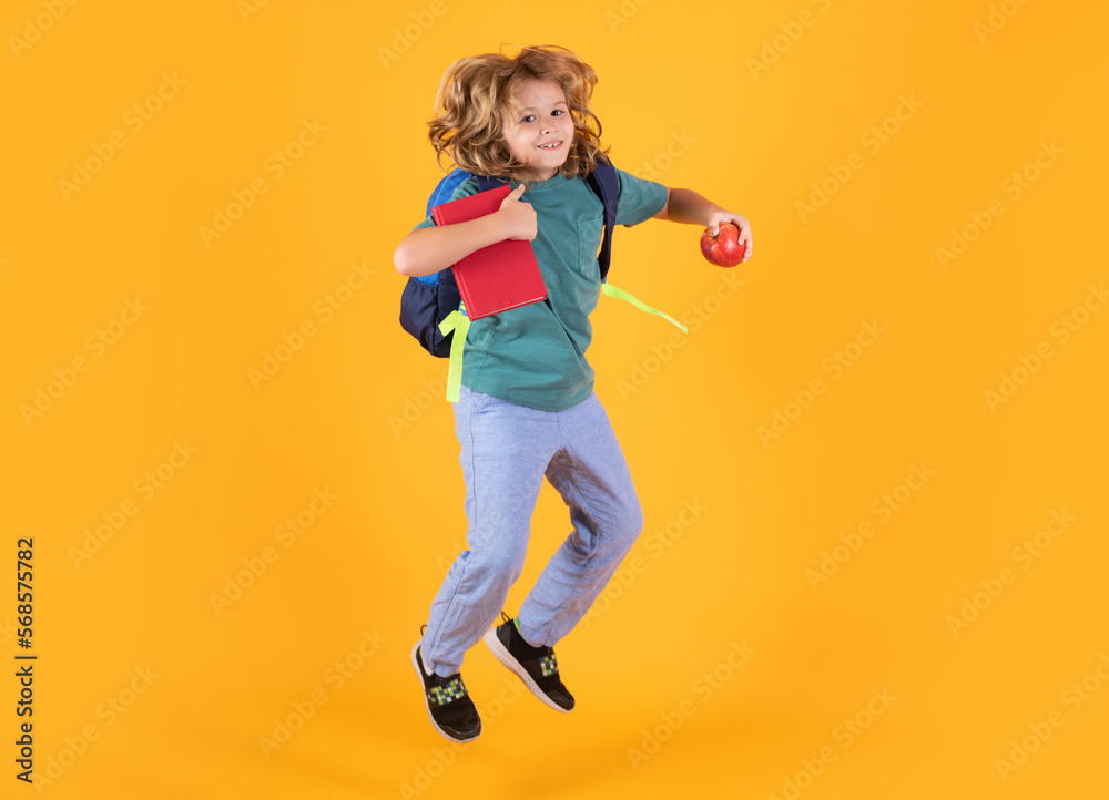 Kid jump and enjoy school. Photo of excited little school jumping holding book, empty space isolated yellow background. Amazed school child jump with backpack.