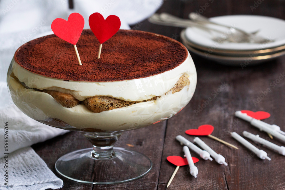 Traditional Italian dessert tiramisu served in a glass vase decorated with paper hearts.