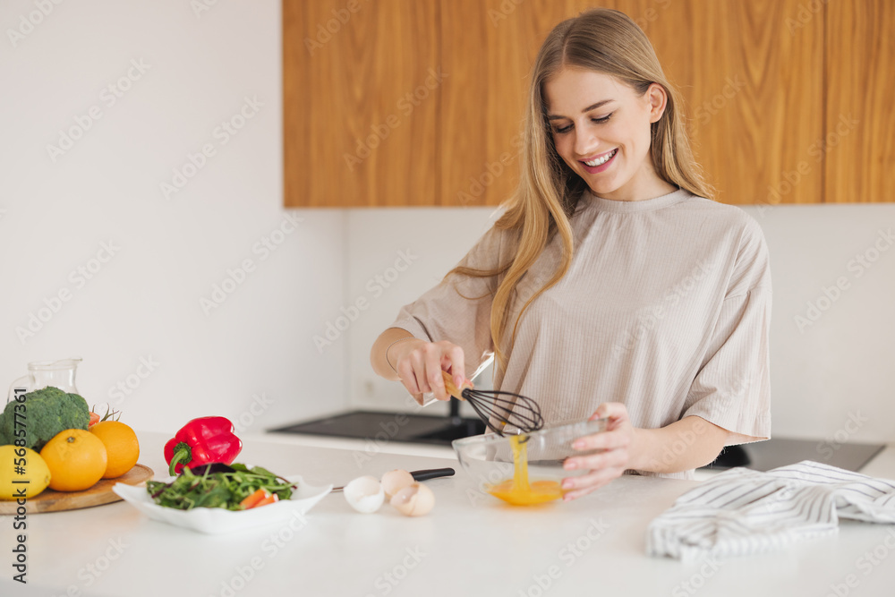 Happy pretty blonde woman in pajamas is preparing breakfast of eggs and fresh vegetables in the kitchen at home. Happy pretty blonde woman in pajamas is preparing breakfast of eggs and fresh vegetables in the kitchen at home.