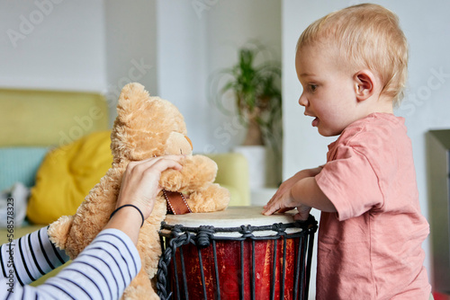 Toddler and teddy bear playing bongo drum together at home photo