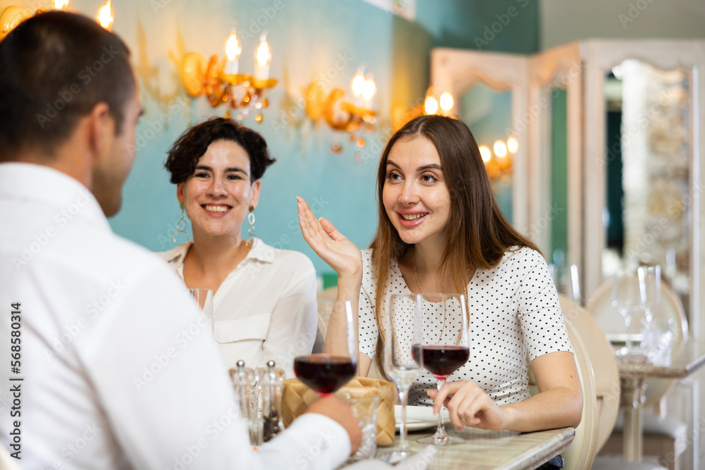 Lady telling story to a man in front of her while sitting with her female friend at the restaurant