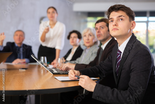 Focused young businessman sitting at table in office, listening attentively to presentation of partners