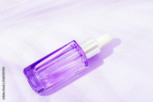 Purple cosmetic face serum bottle on the background with palm leaf shadow in sunlight. Top view, flat lay