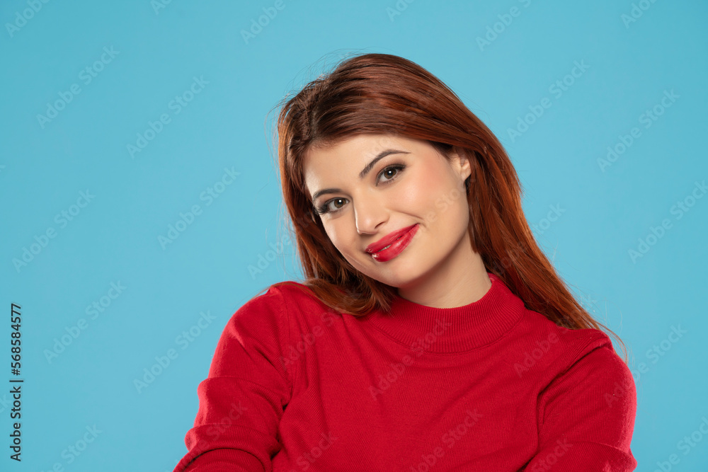 Cheerful gorgeous young woman wearing her ginger long hair smiling happily dressed in red blouse looking at camera with excited joyful smile on a blue background Cheerful gorgeous young woman wearing her ginger long hair smiling happily dressed in red blouse looking at camera with excited joyful smile on a blue background