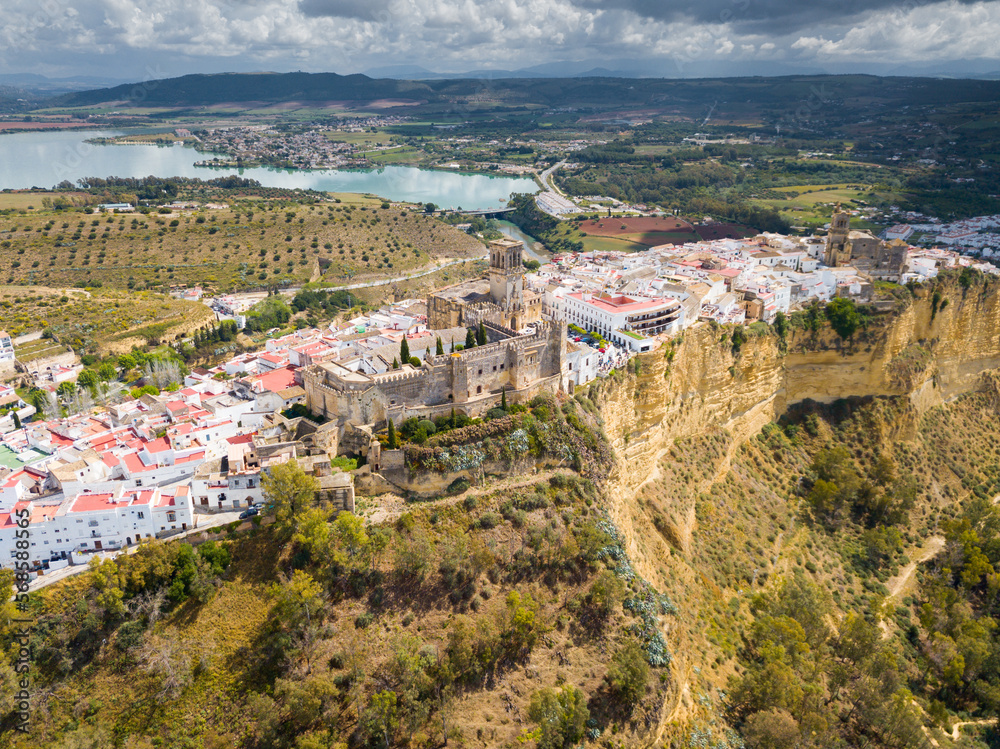 Aerial view of medieval fortified Castle in Andalusian town of Arcos de la Frontera atop sandstone ridge on bank of Guadalete river, Spain
