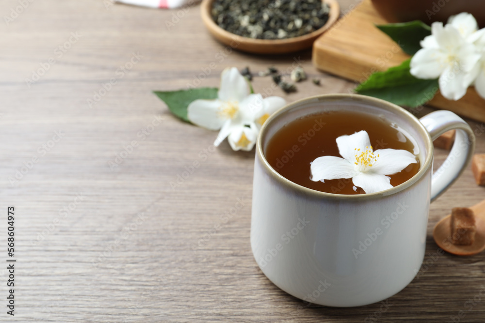 Cup of tea with fresh jasmine flower on wooden table. Space for text Cup of tea with fresh jasmine flower on wooden table. Space for text