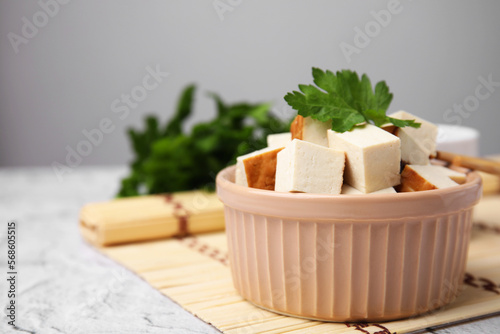 Bamboo mat with bowl of smoked tofu cubes and parsley on white textured table, closeup. Space for text