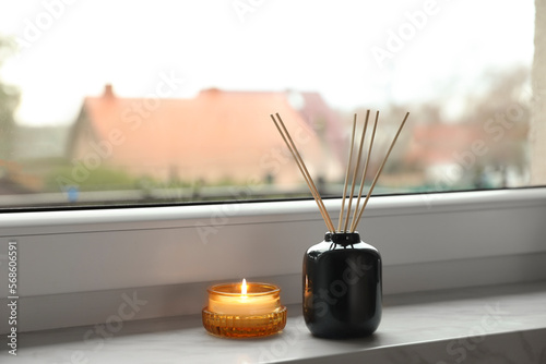 Aromatic reed air freshener and scented candle on windowsill indoors