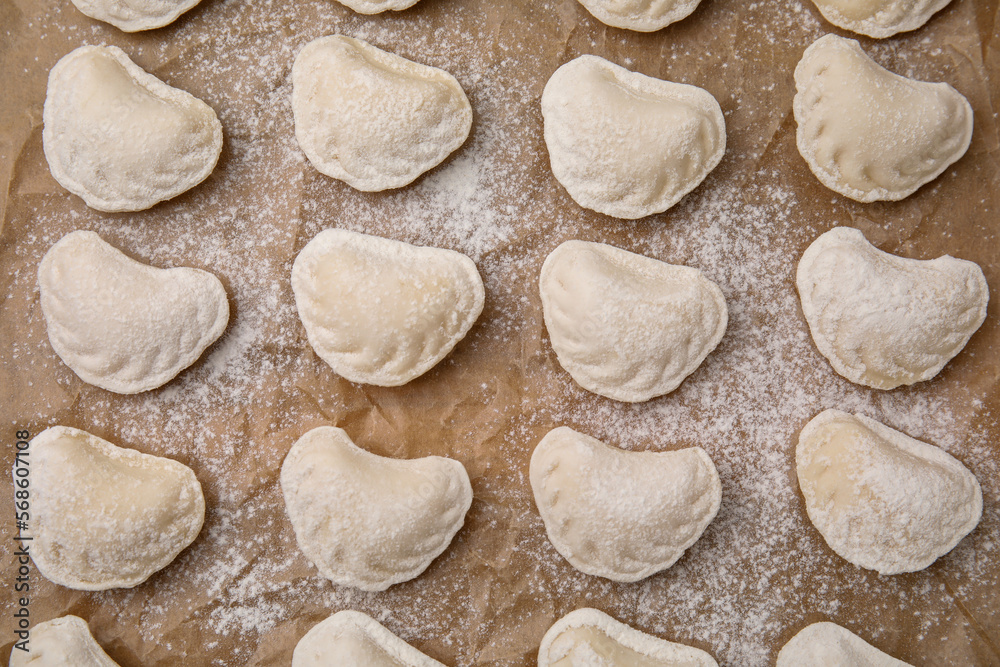 Raw dumplings (varenyky) with tasty filling and flour on parchment paper, top view Raw dumplings (varenyky) with tasty filling and flour on parchment paper, top view