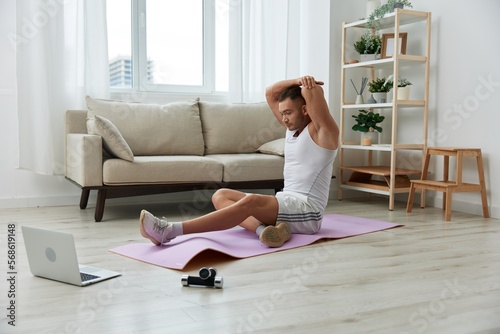 Man sports, watching tape of workout on phone and repeating exercises sports blogger with laptop training online, pumped up man fitness trainer works out at home, the concept of health and body beauty © SHOTPRIME STUDIO