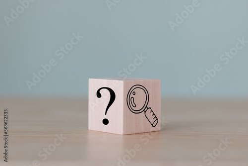 The wooden cube block with an illustration magnifying glass to analyze the question mark sign is isolated on the table. Problems and root cause analysis concept. Define problems to find solutions. photo