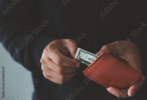 man holding a purse with money cash in the wallet. man looks in the wallet and picks one us dollar banknote. cash spend concept.