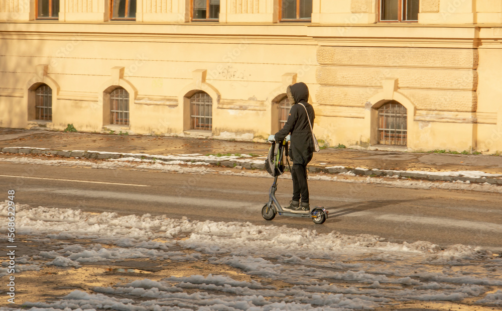 Unrecognizable person riding electric scooter on snowy road in the winter season.