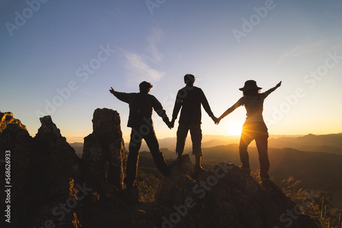 Silhuette Young group praying on the mountain, arms outstretched observing a beautiful dramatic sunrise.