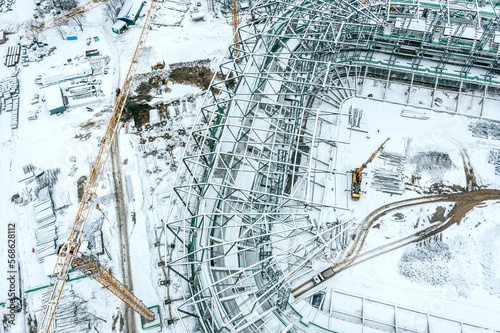 aerial top view of building site, covered by snow with yellow crane. new stadium under construction. photo