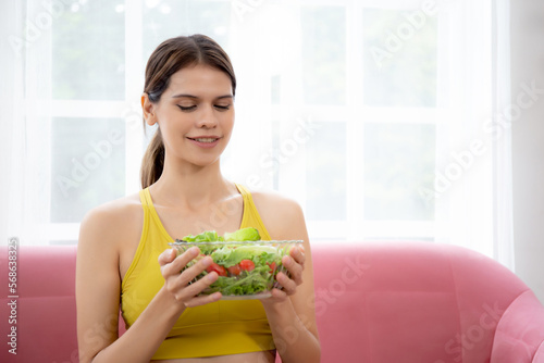 Happy young caucasian woman holding salad vegetable in bowl for eating lettuce in living room at home, female satisfied and vegetarian food for healthy and nutrition, lifestyles and health concept.