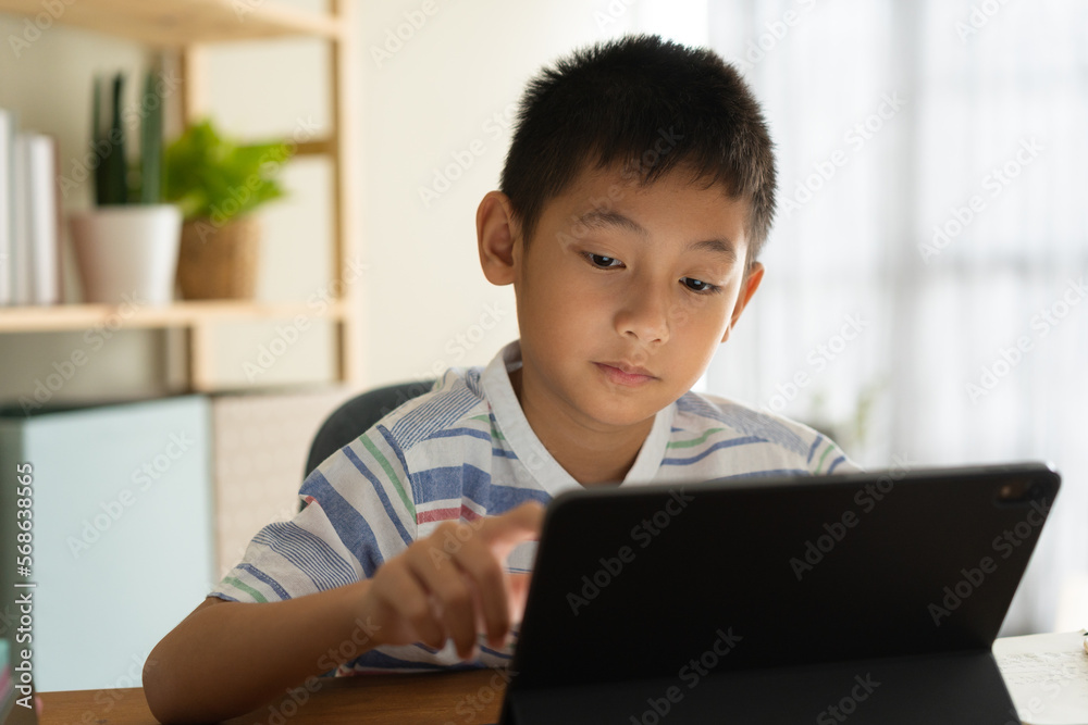 Asian boy is studying online via the internet on tablet at home Asian boy is studying online via the internet on tablet at home