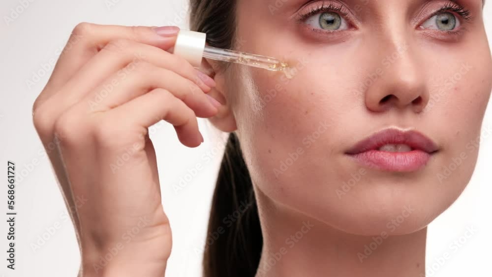 Close up portrait of beautiful female using pipette with serum. Healthy Beauty face on light background at studio. Beautiful female model with natural makeup using face oil with pipette. Skincare. Close up portrait of beautiful female using pipette with serum. Healthy Beauty face on light background at studio. Beautiful female model with natural makeup using face oil with pipette. Skincare.