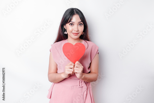 A portrait of a happy Asian woman wearing a pink blouse, holding a red heart-shaped paper isolated by white background photo