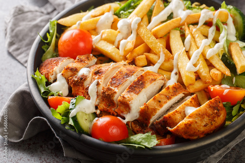 Warm Pittsburgh salad with chicken breast, french fries, vegetables, cheese and lettuce close-up in a bowl on the table. horizontal
