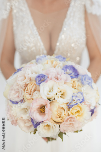 Vertical photo of bridal bouquet with seasonal flowers in white, ivory and purple colors at weding ceremony 