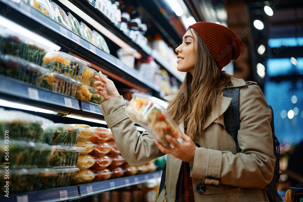 Young woman choosing packed food at refrigerated section in supermarket.