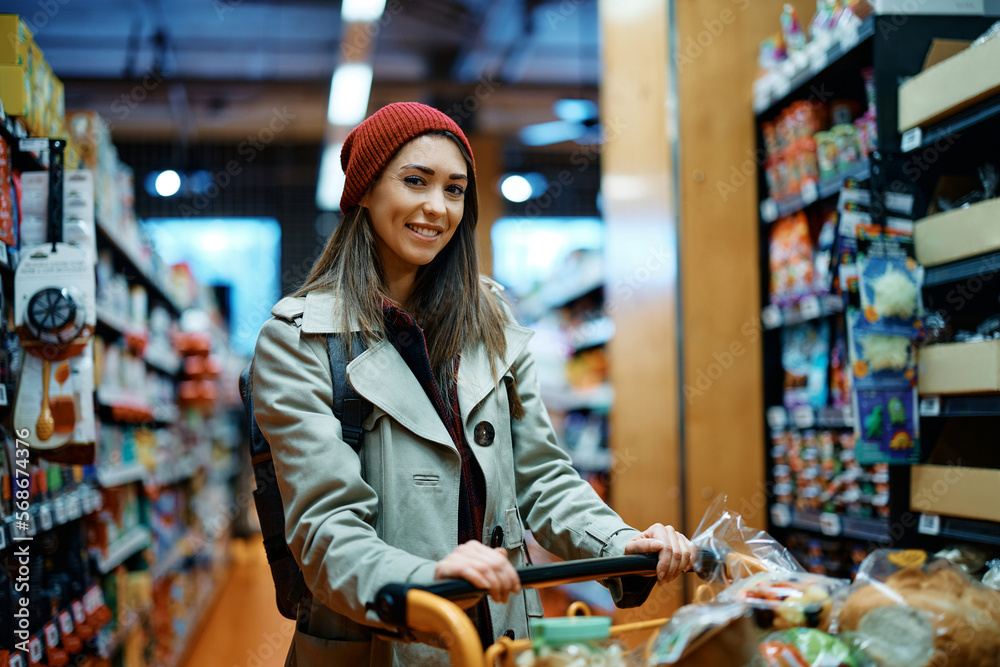 Young happy woman buying groceries in supermarket and looking at camera.