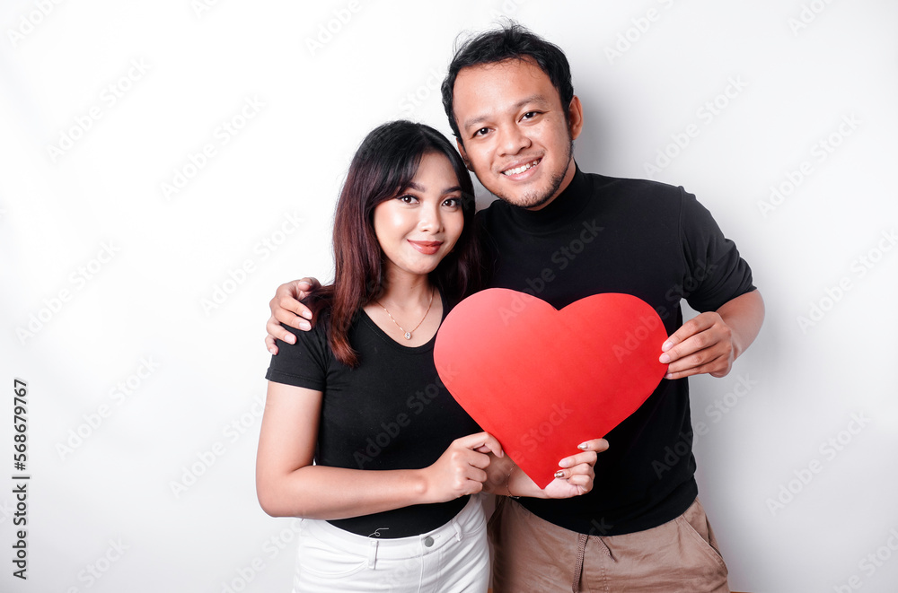 A young Asian couple smiling and holding red heart-shaped paper, isolated by white background