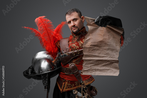 Shot of musketeer from renaissance period with map and helmet against gray background.