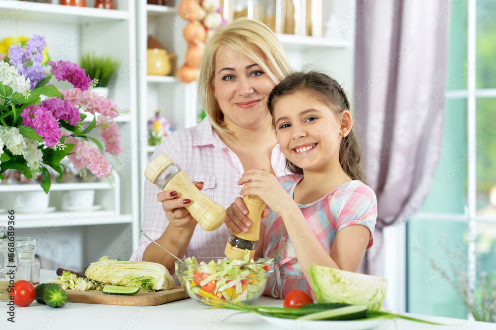 Cute little girl with her mother cooking together at kitchen table Cute little girl with her mother cooking together at kitchen table