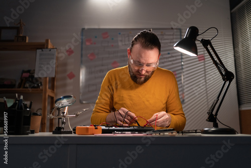 Man testing laptop motherboard using multimeter working in his workshop in the evening. photo