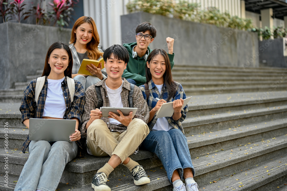 Group of happy young Asian college students sitting on stairs, smiling and looking at the camera.