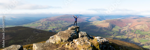 Woman standing with arms raised at top of hill photo