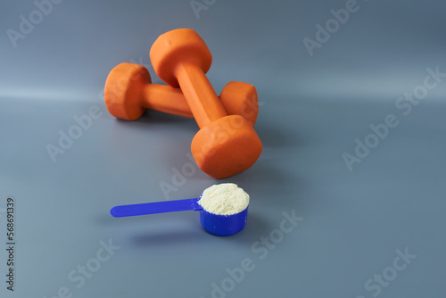 Dumbbells for training in orange with a portion of vanilla protein on a gray background. The concept is sports nutrition supplements. 