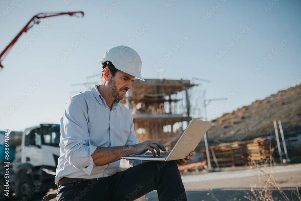 Mature architect working on laptop in construction area Mature architect working on laptop in construction area