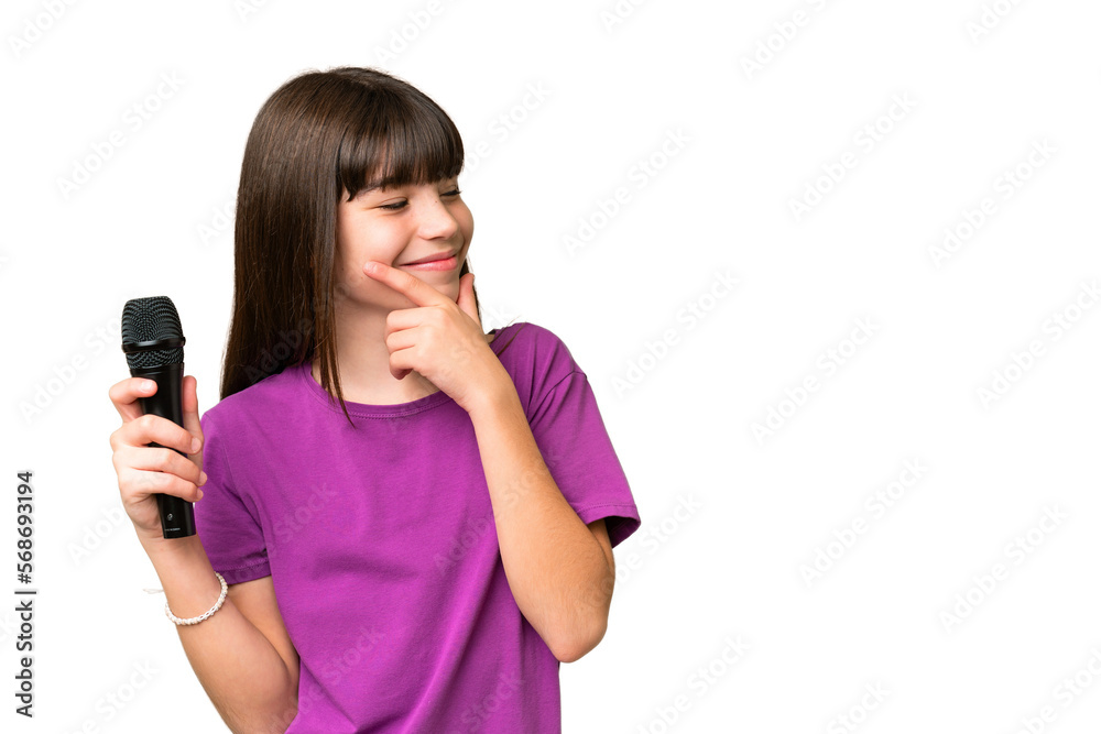 Little singer girl picking up a microphone over isolated background thinking an idea and looking side Little singer girl picking up a microphone over isolated background thinking an idea and looking side