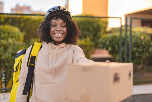 Happy delivery woman wearing cycling helmet giving package photo