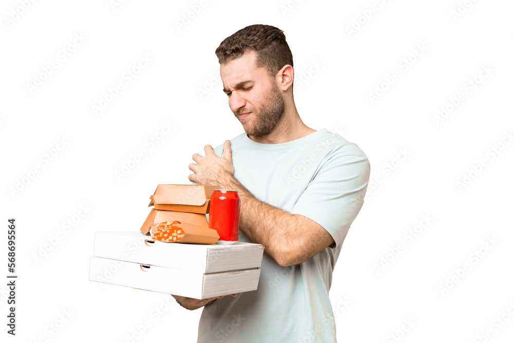 Young handsome blonde man holding pizzas and burgers over isolated background suffering from pain in shoulder for having made an effort Young handsome blonde man holding pizzas and burgers over isolated background suffering from pain in shoulder for having made an effort