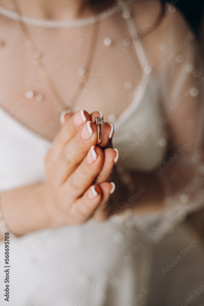 Obraz premium Hands of the bride in a white wedding dress with a gold engagement ring with a diamond close-up. Bride touches the ring with her fingers