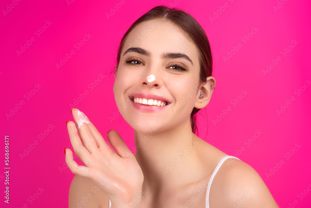 Skin care. Beauty portrait of a beautiful woman applying face cream isolated on studio background. Young spa model uses body care cream. Facial cream, moisturizing lifting nourishing creme.