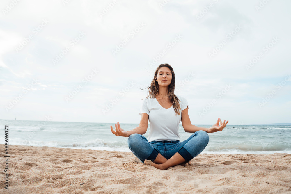 Woman practicing lotus position sitting cross-legged on sand at beach Woman practicing lotus position sitting cross-legged on sand at beach