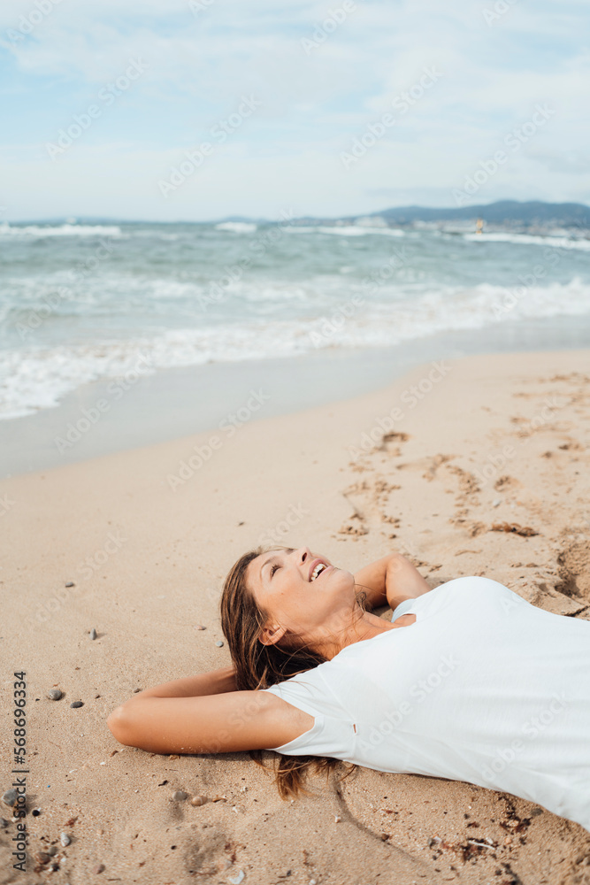 Woman with hands behind head lying on sand by sea at beach Woman with hands behind head lying on sand by sea at beach