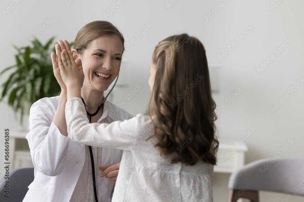 Fototapeta premium Happy female kids doctor working with little patient girl, giving high five greeting gesture to healthy child after medical checkup, healthcare examination, clapping hands, smiling, laughing